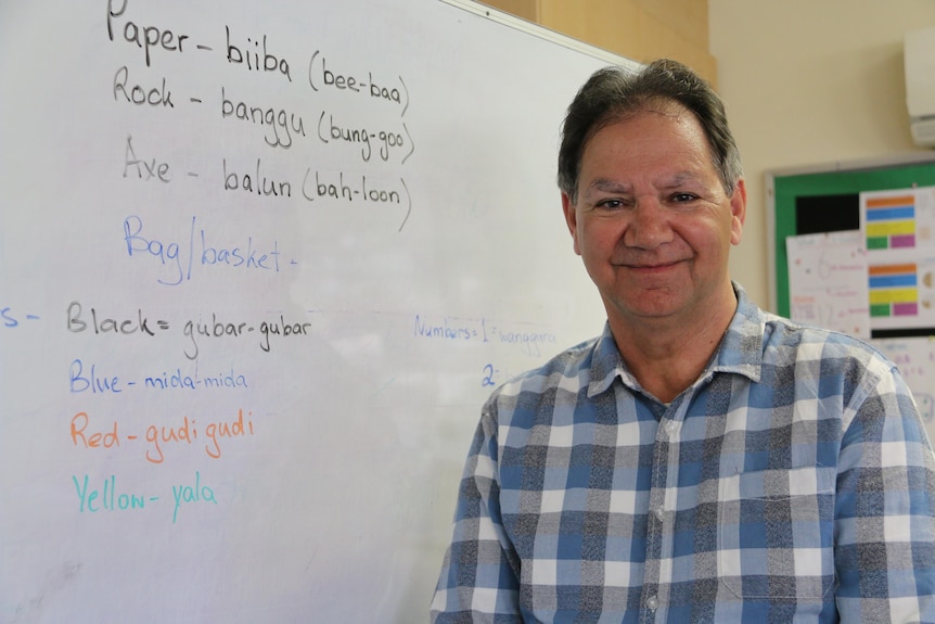Aboriginal man smiling at the camera with a whiteboard with Indigenous language in the background. 