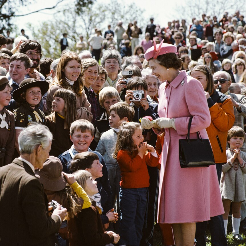 The queen talking to a large group of people, children smiling