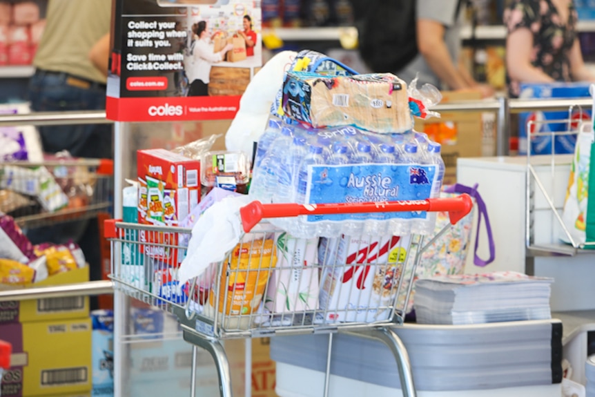Un carrito de la compra lleno de agua embotellada, cereales y otros productos básicos.