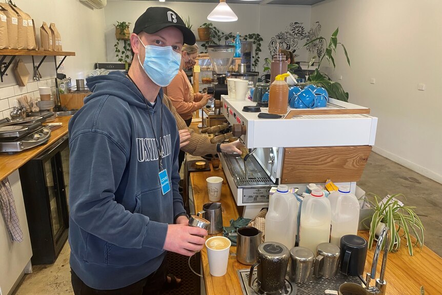 Man wearing mask preparing coffee in cafe
