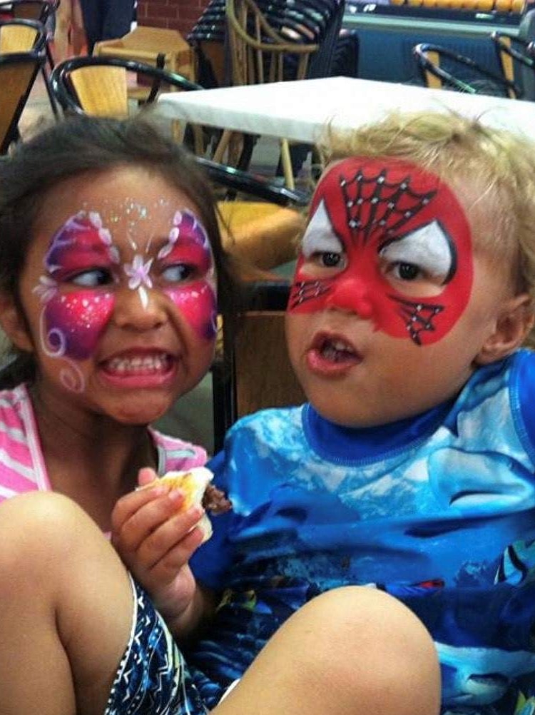 A girl and boy both with faces painted sit at a cafe.