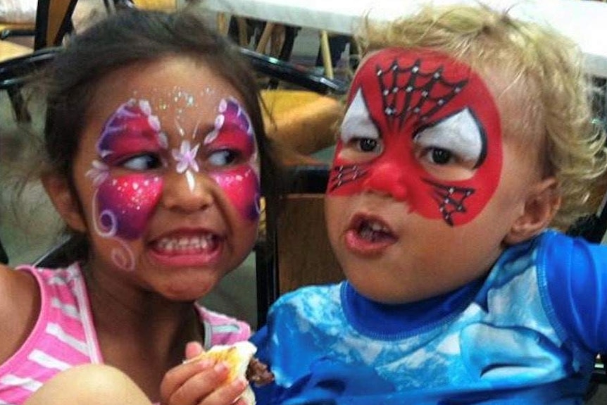 A girl and boy both with faces painted sit at a cafe.