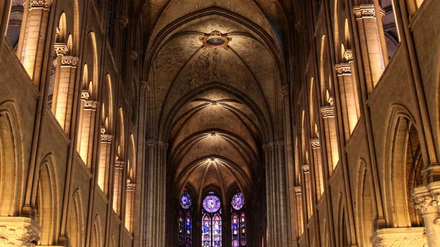 The nave of a cathdral is illuminated as sunlight comes in through stain glass windows in the distance