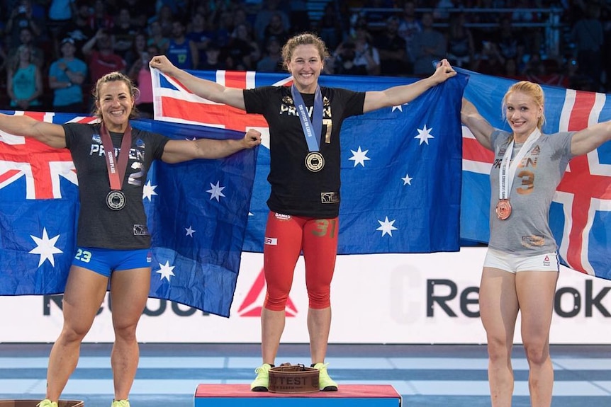 Three woman with each with their country's flag held behind them on the first, second third podium.