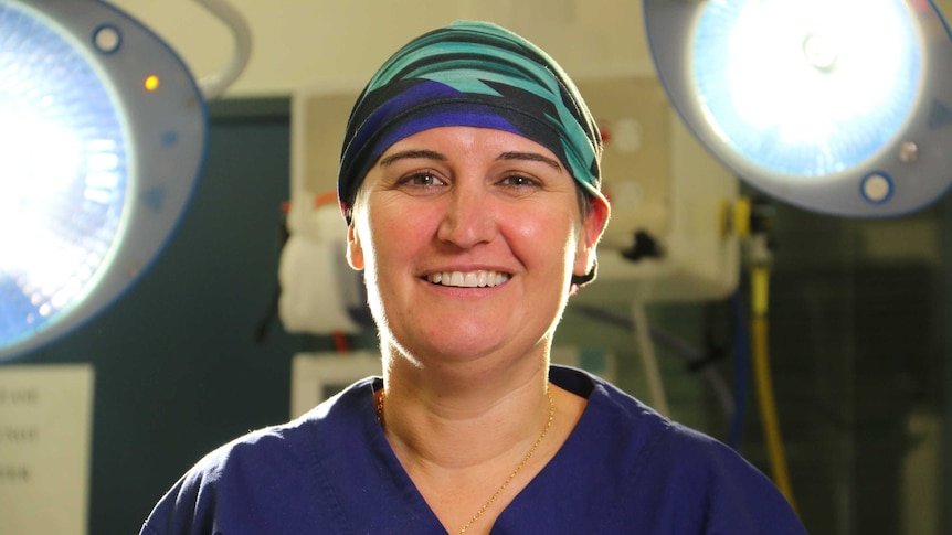 A doctor in scrubs stands in front of operating theatre lights