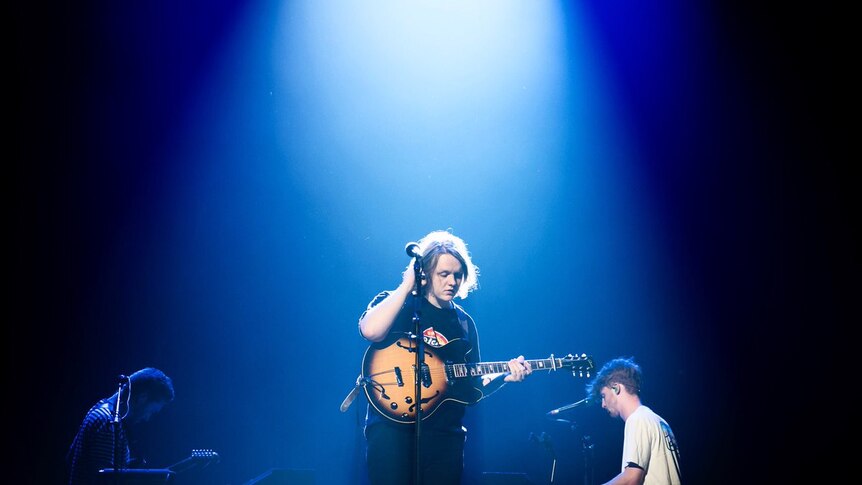 Lewis Capaldi on stage with a guitar standing behind a mic stand