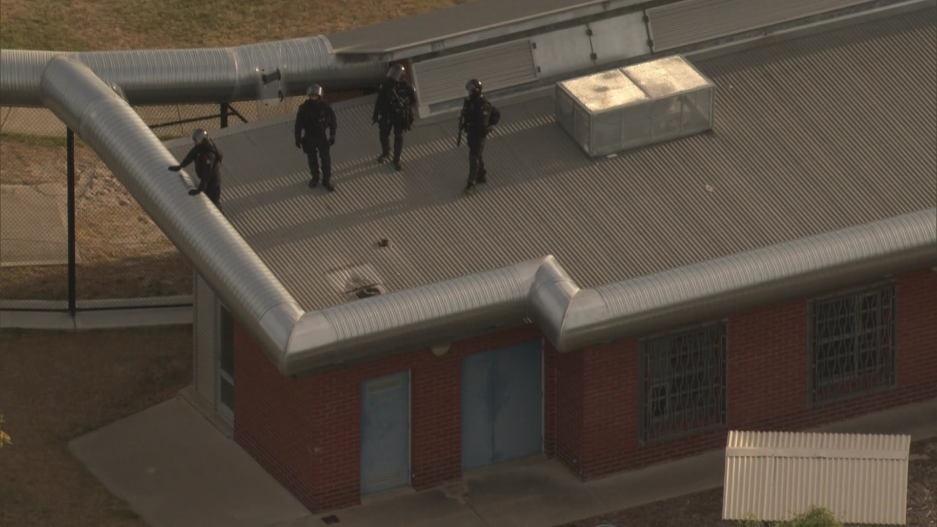 Officers in tactical gear on the roof of a prison building. 