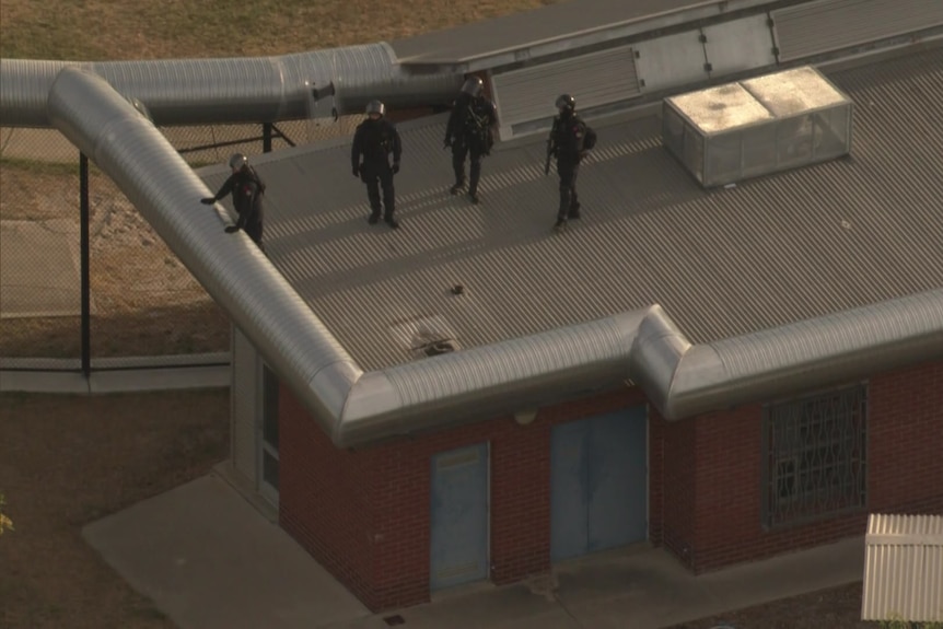 Officers in tactical gear on the roof of a prison building. 