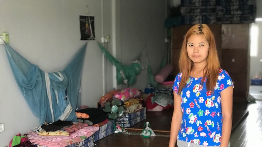 19 year old garment worker Ohn Mar Khaing in a room with folded mattresses, clothes and mosquito nets