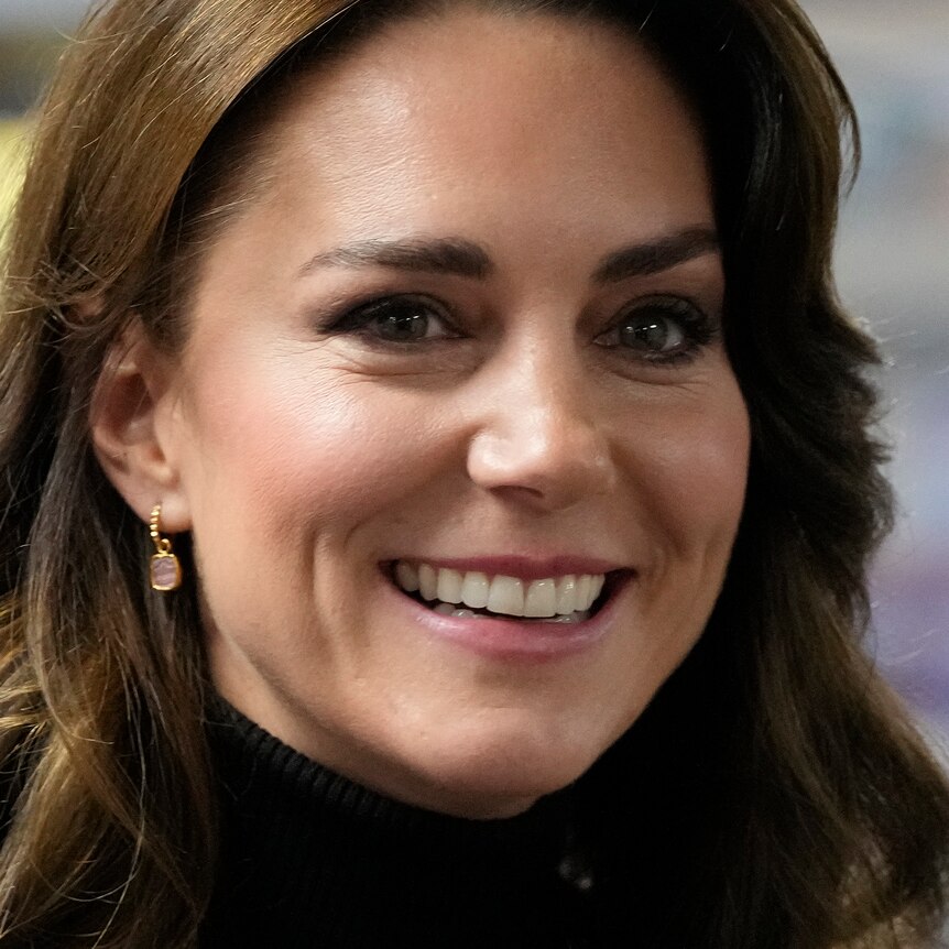 A close up of Kate Middleton smiling while wearing dangly earings.
