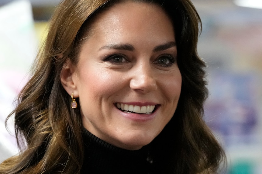 A close up of Kate Middleton smiling while wearing dangly earings.