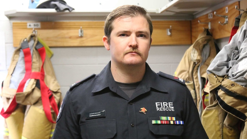 Thurston Darcy standing in a room with firefighting uniforms hanging behind him.