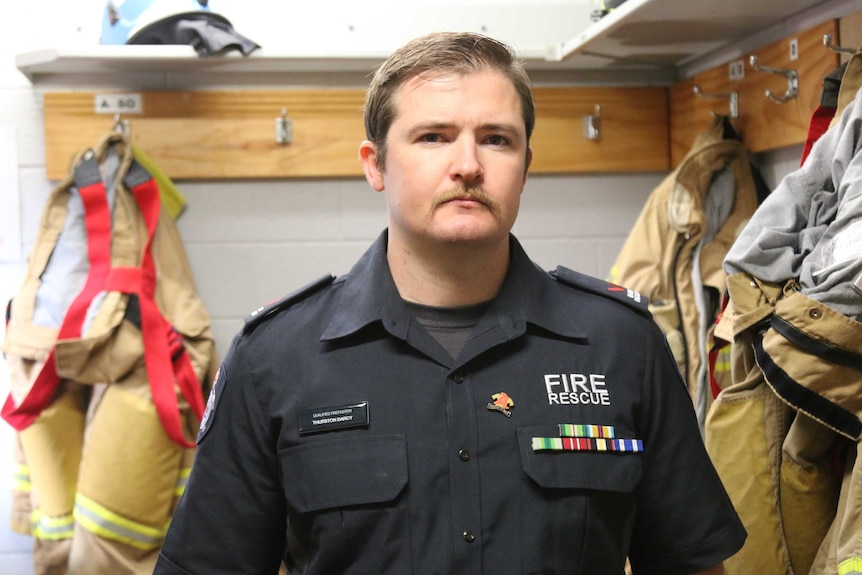 Thurston Darcy standing in a room with firefighting uniforms hanging behind him.