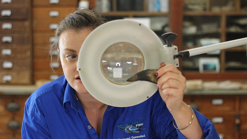 A woman looks at a fossilised tooth through a large magnifying glass.