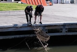 Two men pull a trolley out of a river using ropes.
