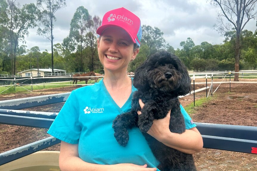 Dr Tess Salmond smiles in front of a stable holding a dog.