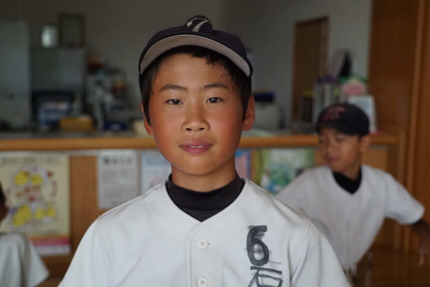 A young Japanese boy wearing a baseball uniform looks into the camera.