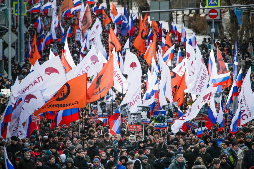 Thousands of people holding flags march down a street in Moscow.