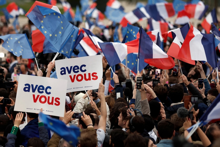Supportes of a victorious political candidate wave French, EU and campaging flags that say "with you" in French.