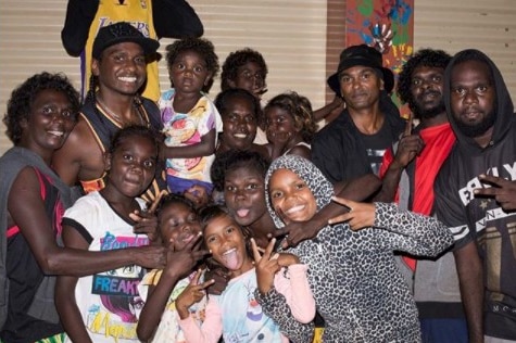 Danzal Baker, aka Baker Boy, smiles among a tight group of young kids, who gesture to the camera