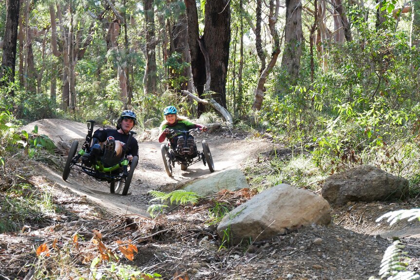 Two people riding adaptive bikes on a curved trail. 