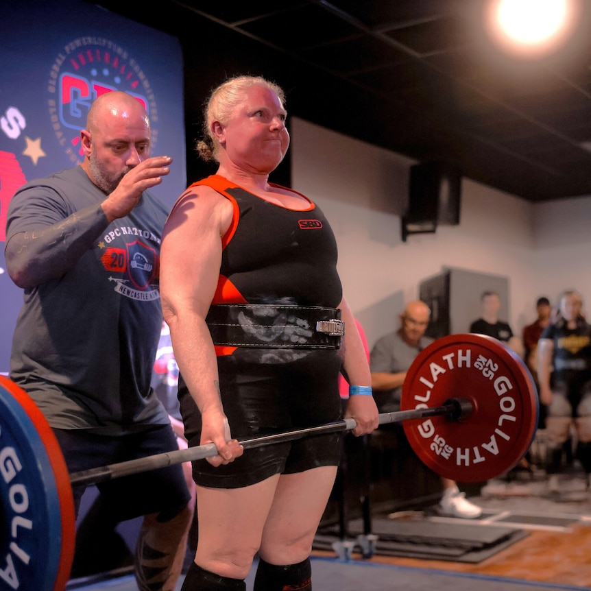 a women with a focused expression picking up 115 kilograms of weights.