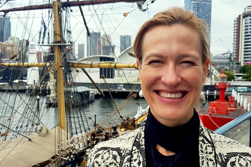 Emily smiles at the camera with a tall ship docked behind her.