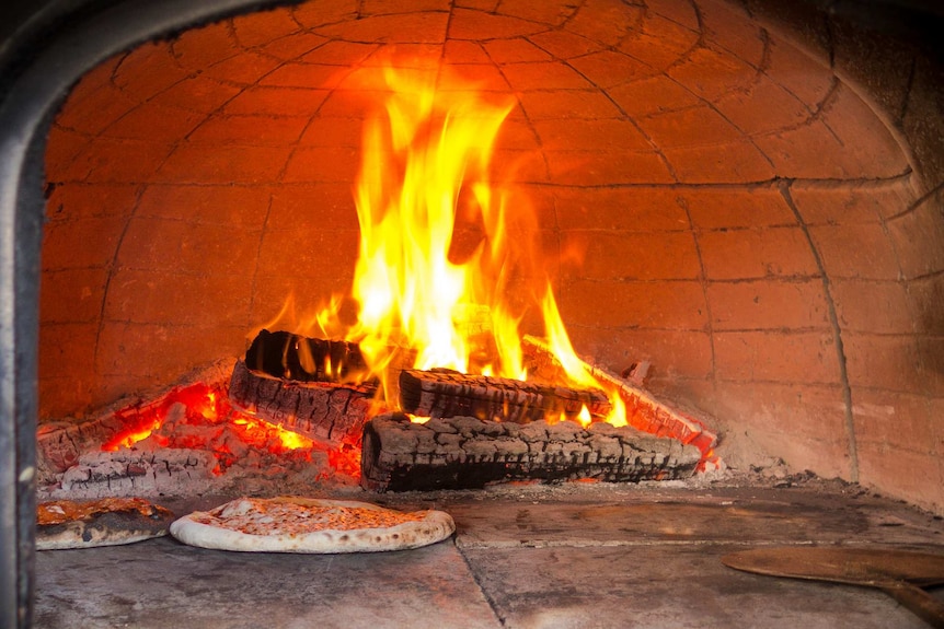 Pizza dough resting inside a pizza oven filled with fire and coals.