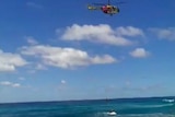Helicopter is over the ocean winching a man and his cat to safety.