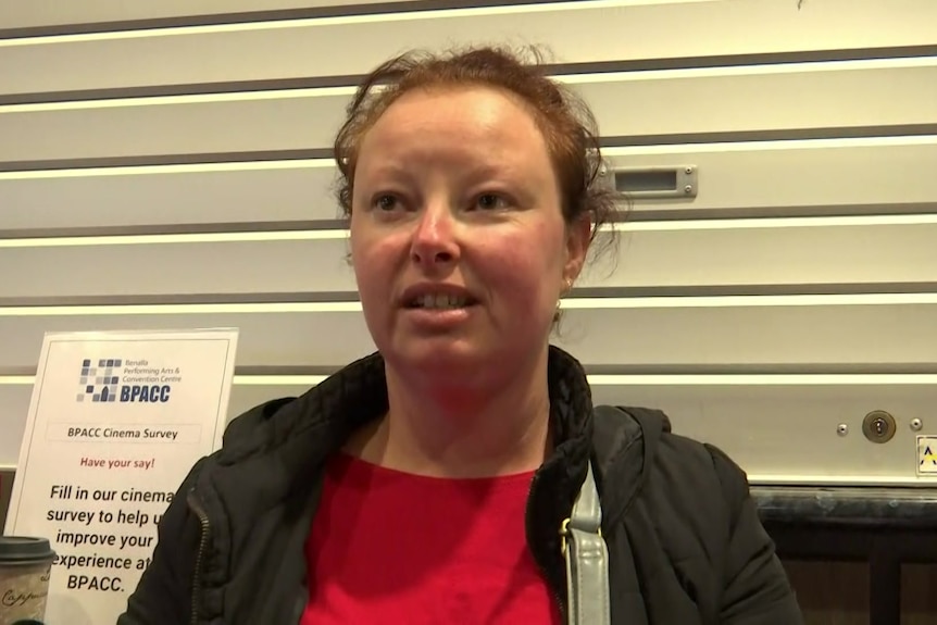 Cilla wears a red shirt and black jacket and sits in a chair at the evacuation centre