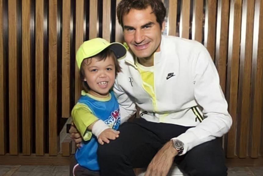 A child with dwarfism stands next to Roger Federer