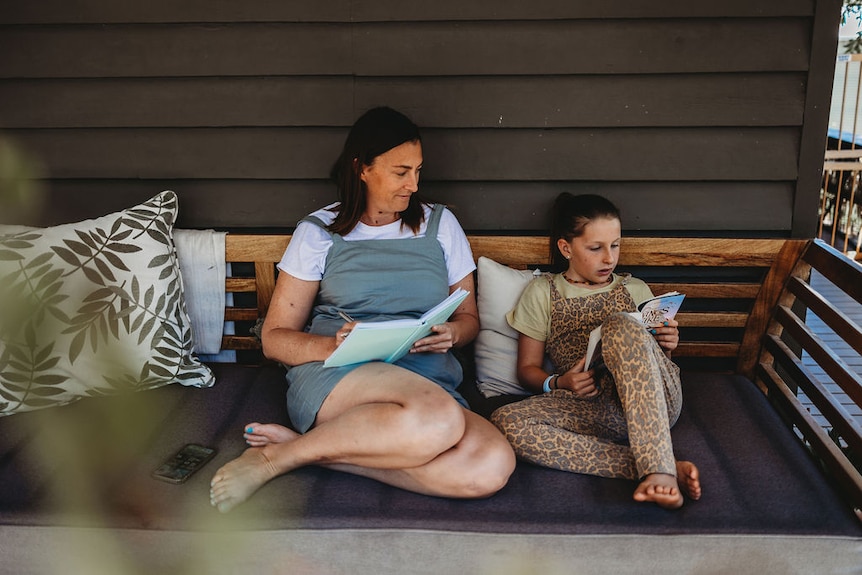 An image of Vicci reading with her daughter on a outdoor sofa