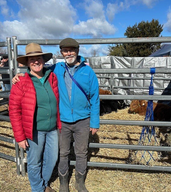 Cattle breeders Anne Waithman and husband Graeme Wilkinson stand in front of a pen of young cows.