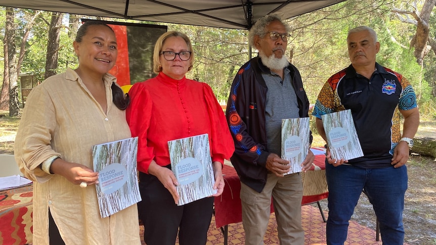 Four indigenous people pose with copies of a report.