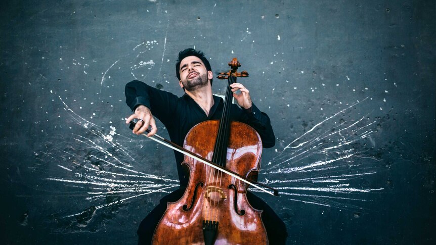 Cellist Pablo Ferrandez playing cello against a dark wall