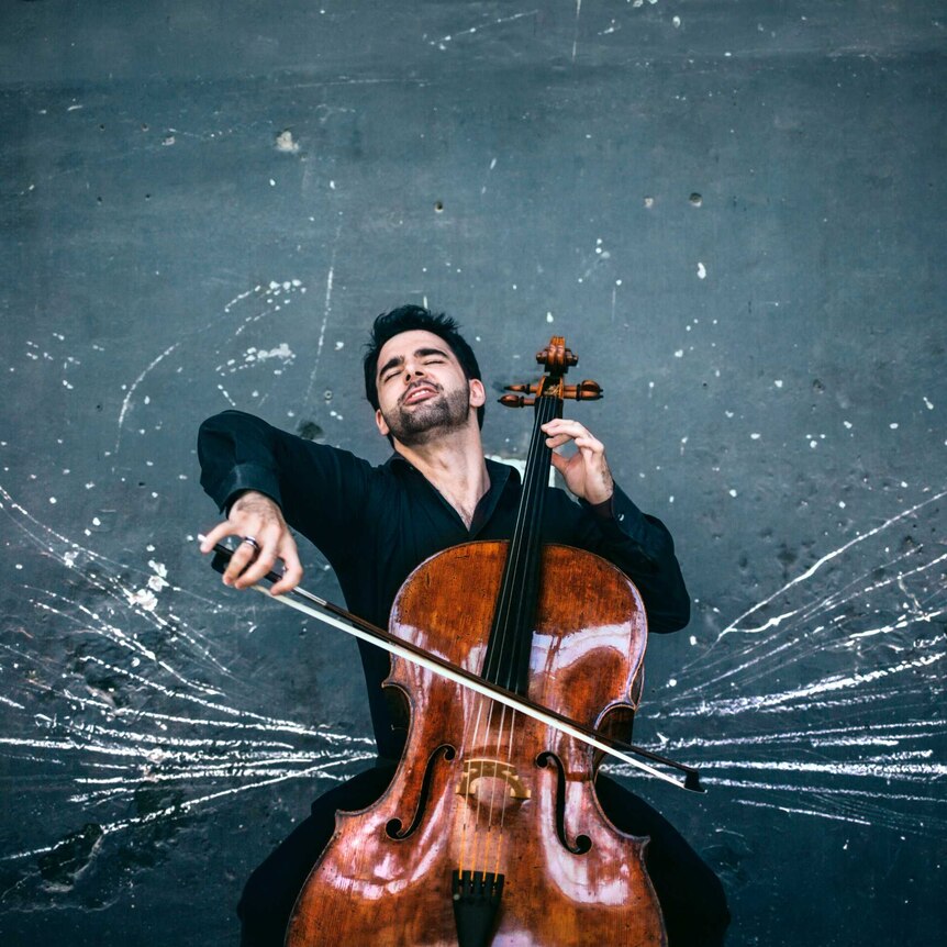 Cellist Pablo Ferrandez playing cello against a dark wall
