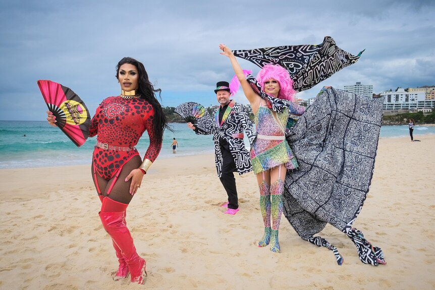 Three people dressed colourful and creative outfits standing on the sand at Bondi Beach