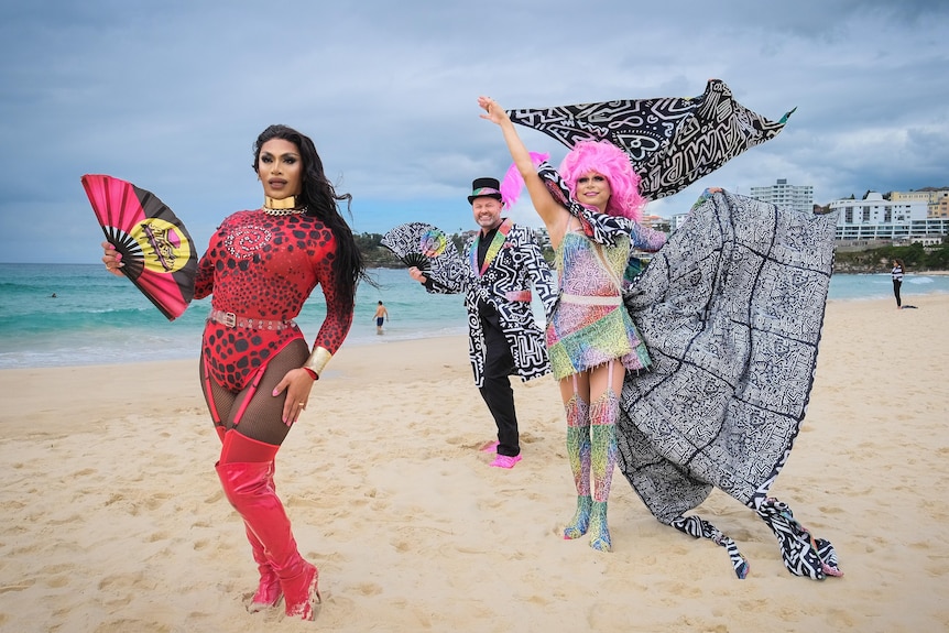 Three people dressed colourful and creative outfits standing on the sand at Bondi Beach