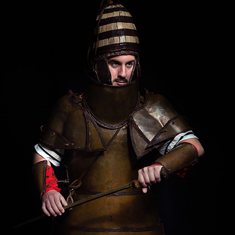 Marine dressed in ancient Mycenean armor poses in a combative stance. 
