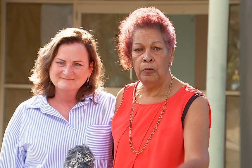 Two women stand arm-in-arm giving a press conference outside a hospital