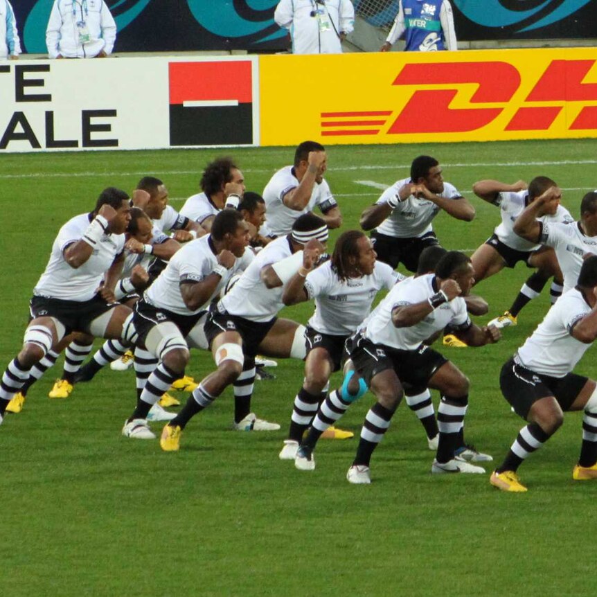 Rugby players wearing a black and white uniform perform a war dance.