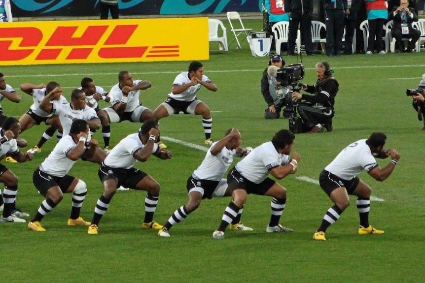 Rugby players wearing a black and white uniform perform a war dance.