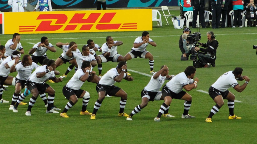 Rugby players wearing a black and white uniform perform a war dance.