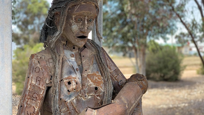 A metal sculpture of a woman standing with her mouth open, holding a baby.