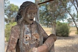A metal sculpture of a woman standing with her mouth open, holding a baby.