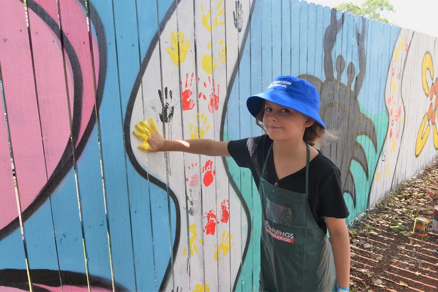 Young child adds handprint in paint to colourful laneway mural.