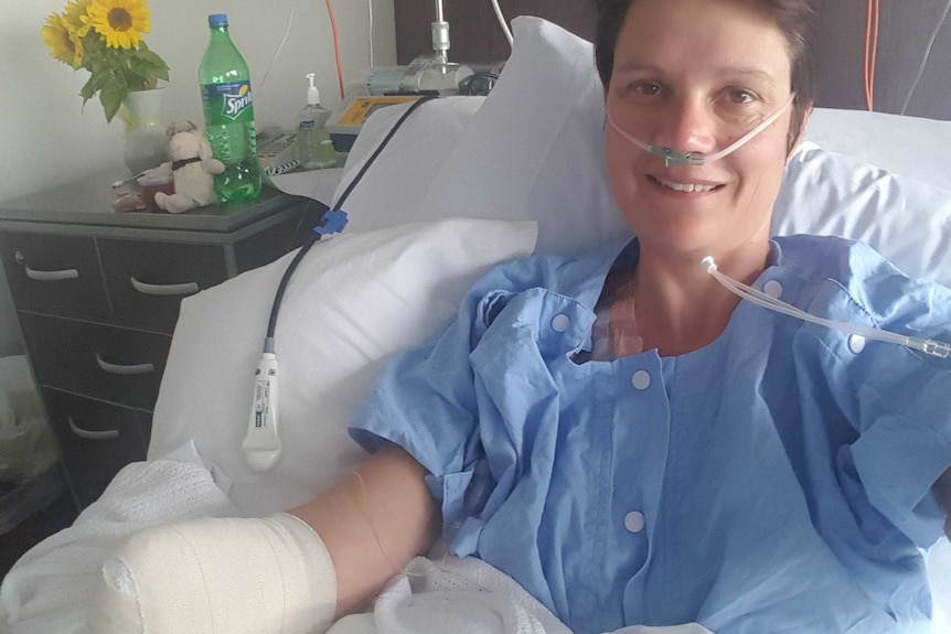 A woman in a hospital bed showing bandages over the end of her right arm.