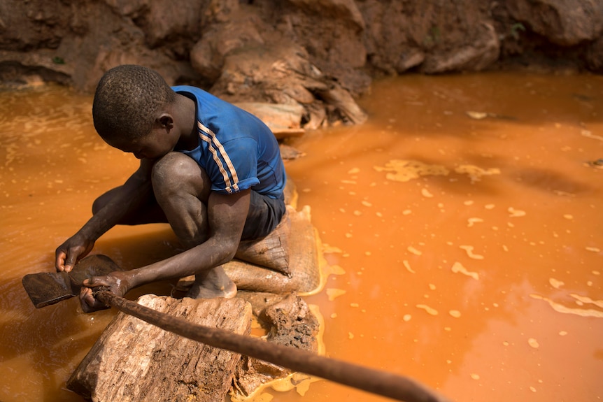 A young boy crouches in muddy water with a shovel