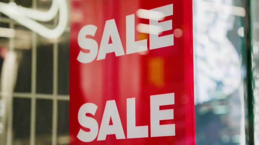 A red sign with white block letters that read "Sale" in a shop front window.