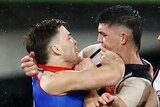 Two AFL players come together in a melee, showing anger with each other.